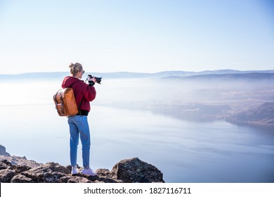 Back View Of Full Body Of Female Photographer With Backpack And Photo Camera Taking Picture Of Amazing Scenery With Foggy Landscape And River In Sunny Day