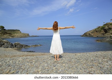 Back view full body portrait of a woman in white dress stretching arms on the beach