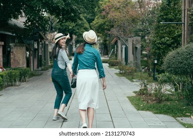 back view full length of young excited girl in denim overalls walking and hands holding friend on street. beautiful lady tourist sharing happiness with sister during travel in Tokyo Japan in spring