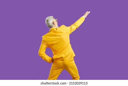 Back view of funny energetic senior man in stylish outfit having fun at party. Backview of cheerful elderly guy wearing bright yellow party suit dancing isolated on solid purple colour background - Powered by Shutterstock