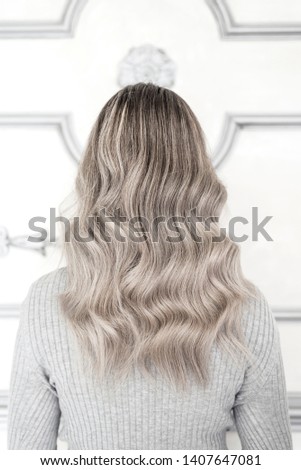 Back view of girl with beautiful blond sombre hairstyle standing in hair salon, Balayage technique concept