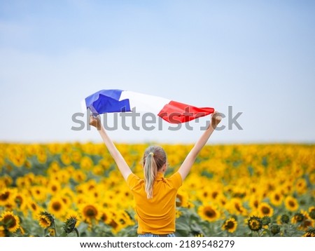 Back view of girl holding flag of France in the sunflower field. National holidays concept: Armistice day, Bastille day, Victory day, Labour day. Beauty of France. Selective soft focus.