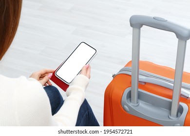 Back view of girl holding smartphone with white blank screen mockup. Traveler with phone at the airport with passport and suitcase. Lifestyle concept with digital technology.
