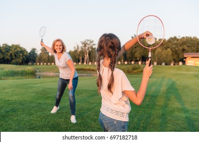 back view of girl playing badminton with grandmother on green lawn