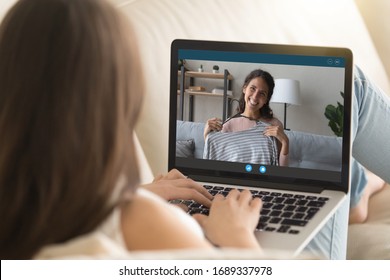 Back View Of Girl Relax On Couch At Home Talk On Video Call With Smiling Sister Or Friend On Quarantine, Young Woman Have Fun Chat Communicate Online Use Webcam Conversation On Modern Laptop