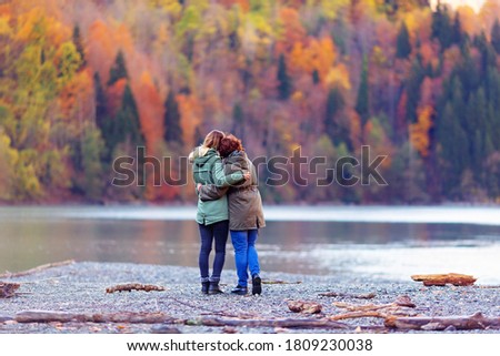 Back view of girls looking at autumn mountains and lake admiring beautiful sunset view