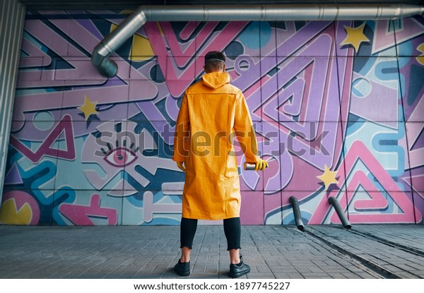 Back view of graffiti painter looking\
to the wall with his paintings. Street art\
concept