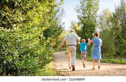 Back View Of Grandparents And Grandchild Jumping On A Nature Path