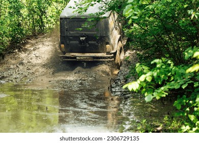 Back view of green russian off-road utility vehicle UAZ Hunter going up dirty road, crossing river stream in summer forest among trees. Racing, travelling, extreme trip, four wheel drive, adventure.