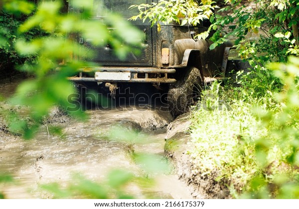 Back view of green russian off-road utility\
vehicle UAZ Hunter going up dirty road, crossing river stream in\
summer forest among trees. Racing, travelling, extreme trip, four\
wheel drive, adventure.