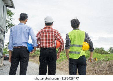 Back View Group Of Engineer, Architect, Supervisor Worker, Green Reflective Vest, Holding Yellow Safety Helmet, Water Level Gauge At Construction Site, Empty Land. Real Estate, Home Building Concept