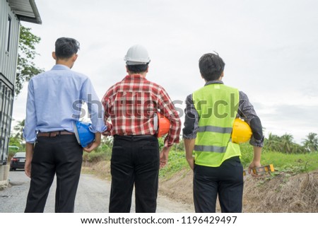 Back view group of engineer, architect, supervisor worker, green reflective vest, holding yellow safety helmet, water level gauge at construction site, empty land. Real estate, Home building concept