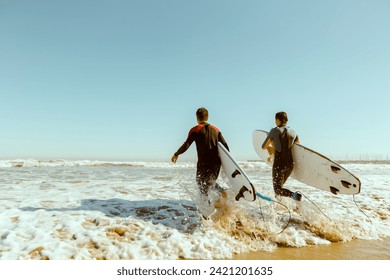 Back view of group of friends with surfboards in wetsuit entering towards ocean for surfing on waves - Powered by Shutterstock