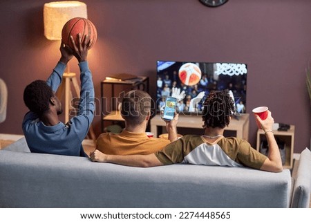 Back view at group of friends watching basketball match at home and drinking beer