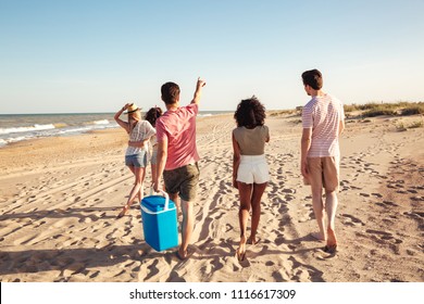 Back view of group of happy young friends in summer clothes going for a picnic at the beach and pointing away - Powered by Shutterstock