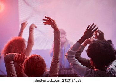 Back view at group of people dancing in neon lights at nightclub with DJ in background - Shutterstock ID 2310484023