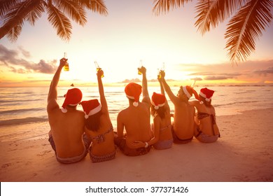 Back View Of Group People With Raised Hands Holding A Bottle Of Beer On Beach, Christmas Holiday