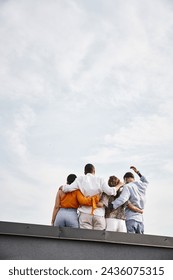 back view of group of young multicultural friends in casual urban attires posing on rooftop