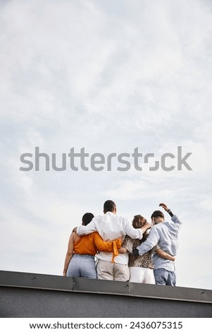 back view of group of young multicultural friends in casual urban attires posing on rooftop