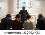 Back view of group of young people praying silently together during Sunday service in Catholic church