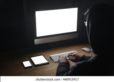 Back View Of Hacker Using Blank Screen Computer, Tablet And Cell Phone In Dark Room