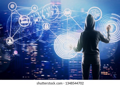 Back view of hacker using glowing interface on blurry night city background. Internet, innovation and communication concept. Double exposure 