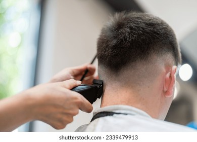 Back view of Hairdresser shaving his client's hair with clipper in salon. Self care, masculine beauty. Barber. Barber girl cuts a man's hair. - Shutterstock ID 2339479913