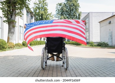 back view of handicapped soldier in wheelchair holding usa flag on city alley