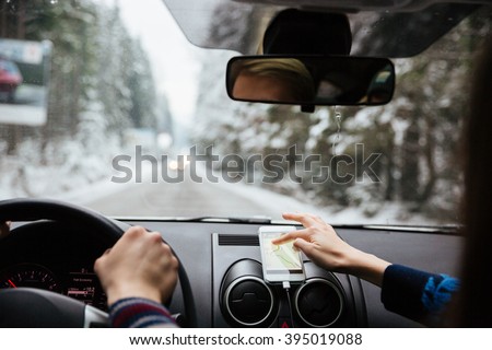 Back view of hands of young couple driving in winter forest and using navigation on mobile phone 