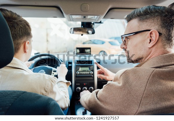 back view of handsome father pointing on\
something while teaching teen son driving\
car