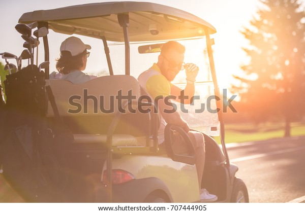 Back view of handsome men driving a\
golf cart, one guy is looking at camera and\
smiling