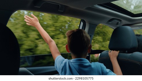 Back view of handsome satisfied blond teen boy which sticks his hand out of car window and waving together with his mother who's is behind the wheel - Powered by Shutterstock