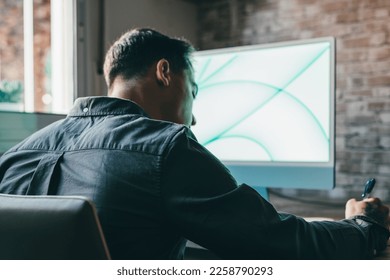 Back view handsome young businessman working with computer remotely, sitting at wooden table in office. Pleasant happy man communicating in social network, searching information online. - Shutterstock ID 2258790293