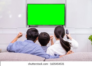 Back View Of Happy Asian Family Watching TV Together In Living Room At Home; Cheerful And Fun With Movie, With Green Screen