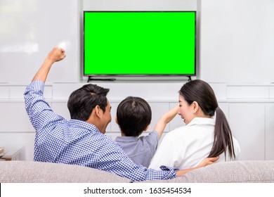 Back View Of Happy Asian Family Watching TV Together In Living Room At Home; Cheerful And Fun With Movie, With Green Screen