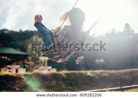 Back view of happy barefoot girl on swing in sun light. Carefree woman