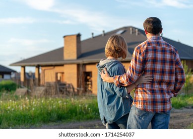 Back view of happy family is standing near their new modern house and hugging 