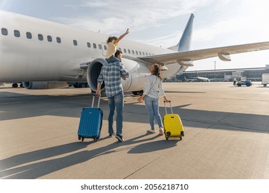 Back view of happy family standing near a large plane with two suitcases outdoor. Trip concept - Shutterstock ID 2056218710