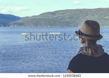 Back view of happy hipster woman in hat standing and looking at river. Traveler enjoying time in nature outdoor lake. Lifestyle travel, relaxation and freedom concept. 