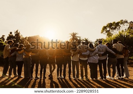 Back view of happy multigenerational people having fun in a public park during sunset time - Community and support concept 