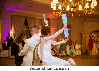 Back View Of The Happy Newlyweds Who Are Playing The Game In The Restaurant And Sitting On The Chairs