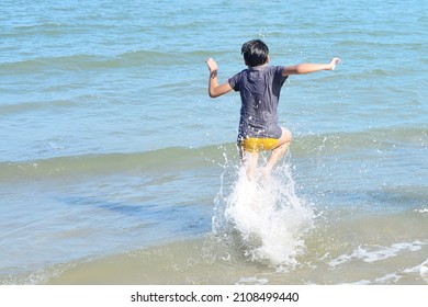 Zurück Blick auf den glücklichen, asiatischen Jungen, der auf dem Strandkinderkind in das Meer strömt und Wellen am Strand genießt