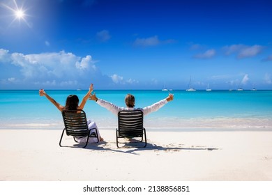 Back view of a happy vacation couple sitting on a tropical beach in the Caribbean and enjoying their summer holidays