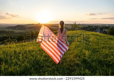 Back view of happy woman with USA national flag standing outdoors at sunset. Positive female celebrating United States independence day. International day of democracy concept.