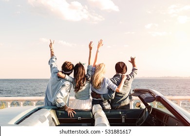 Back view of happy young friends standing with raised hands near the car - Shutterstock ID 531881617