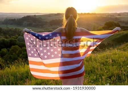 Back view of happy young woman posing with USA national flag standing outdoors at sunset. International day of democracy concept.