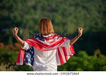 Back view happy young woman posing with USA national flag standing outdoors at sunset. Positive girl celebrating United States independence day. International day of democracy concept.