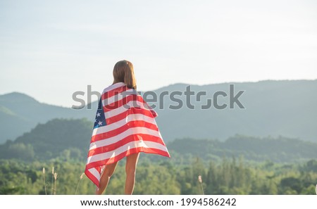 Back view happy young woman posing with USA national flag standing outdoors at sunset. Positive girl celebrating United States independence day. International day of democracy concept.