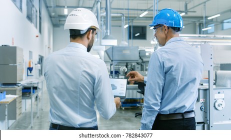 Back View Of The Head Of The Project Holds Laptop And Discussing Product Details With Chief Engineer While They Walk Through Modern Factory.