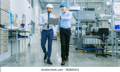 Back View of the Head of the Project Holds Laptop and Discussing Product Details with Chief Engineer while They Walk Through Modern Factory. - Shutterstock ID 782845411